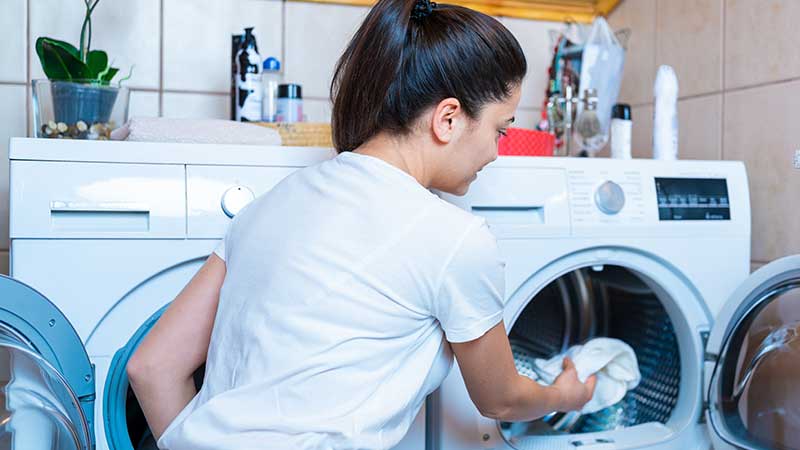 mulher a colocar roupa dentro de máquina de secar roupa